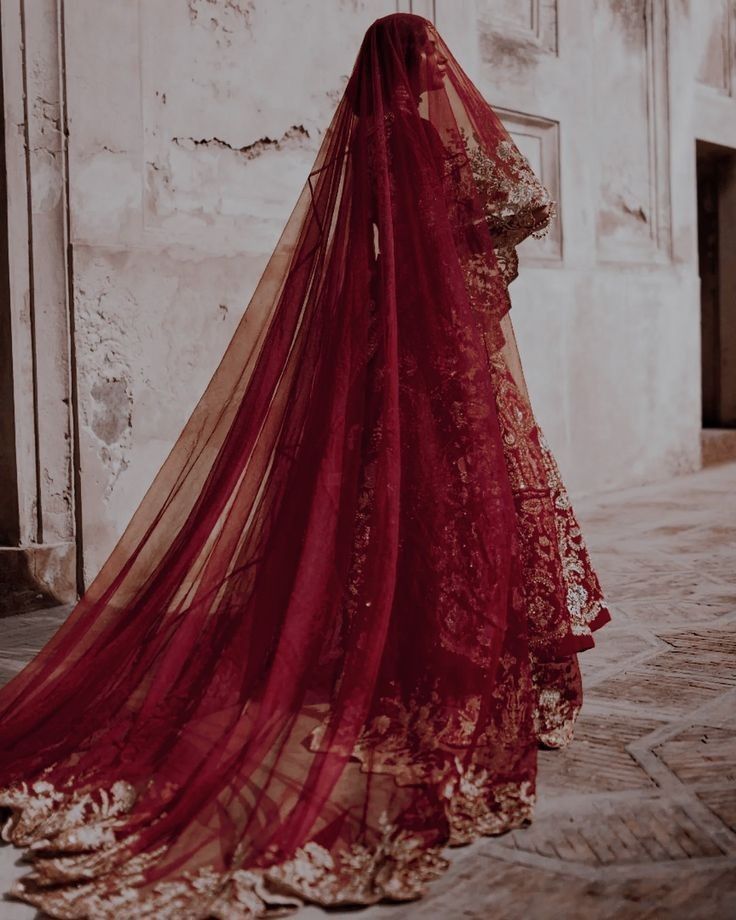 Bride walking away in a deep red embroidered lehenga with a flowing veil trail